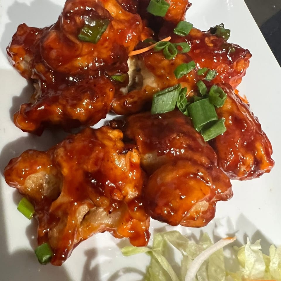 Sweet and sour chicken pieces, garnished with green onions, on a white plate with lettuce.