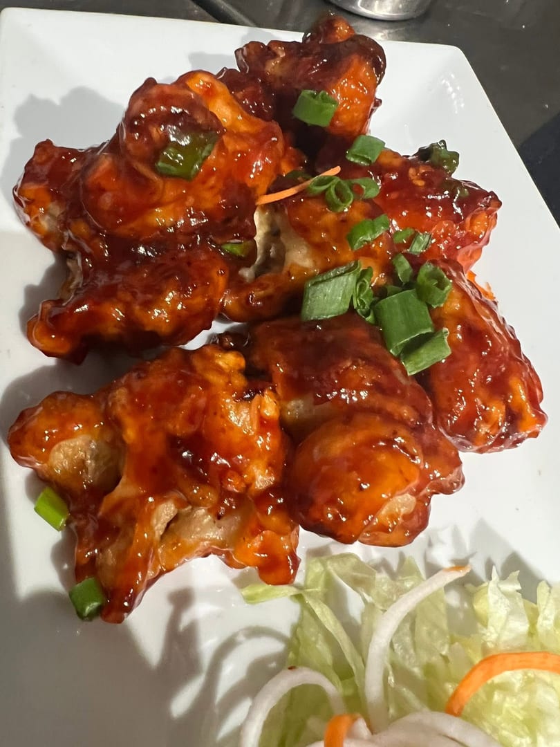 Sweet and sour chicken pieces, garnished with green onions, on a white plate with lettuce.