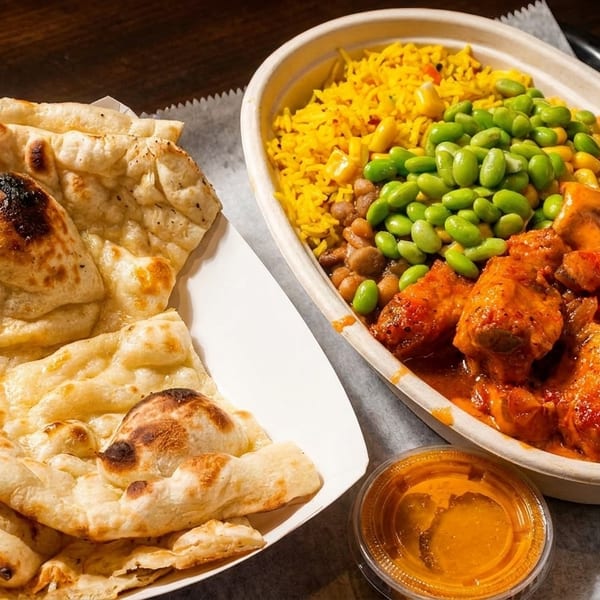 Indian butter chicken with rice, edamame, and naan bread, served with a side of sauce.