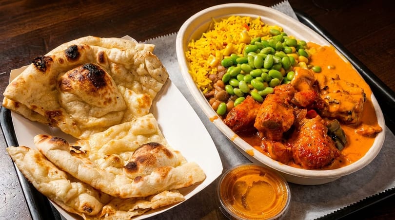 Indian butter chicken with rice, edamame, and naan bread, served with a side of sauce.