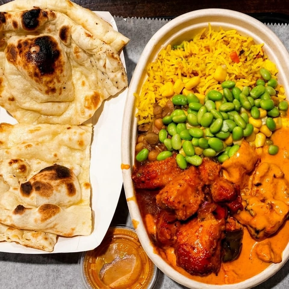 Indian food with naan bread, chicken curry, yellow rice, edamame, and corn on a tray.