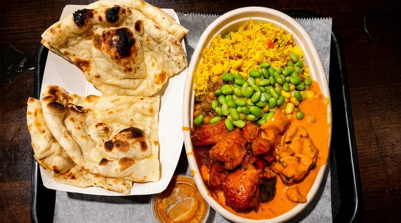 Indian food with naan bread, chicken curry, yellow rice, edamame, and corn on a tray.